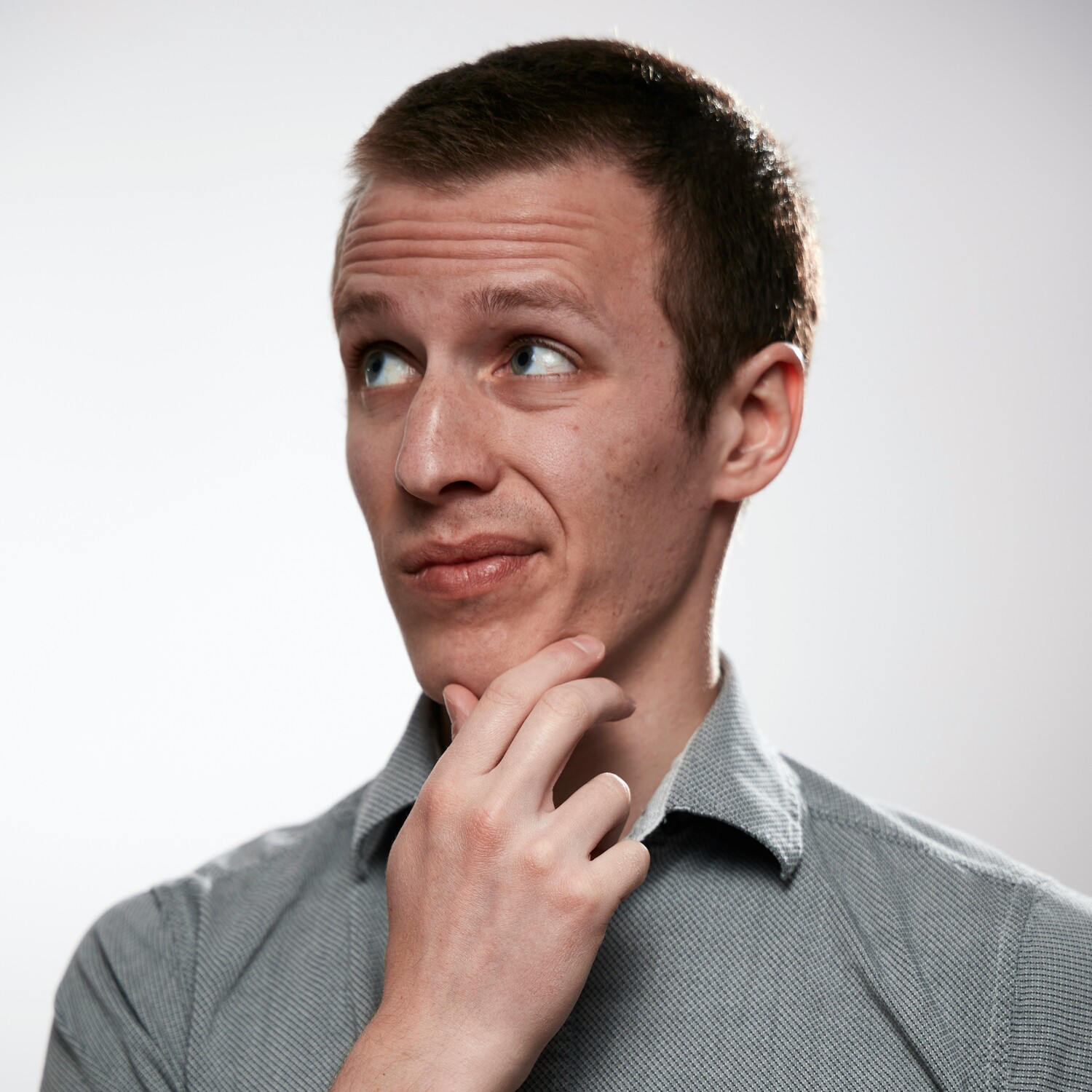 A man in a grey shirt looks dubious with his hand on his chin.
