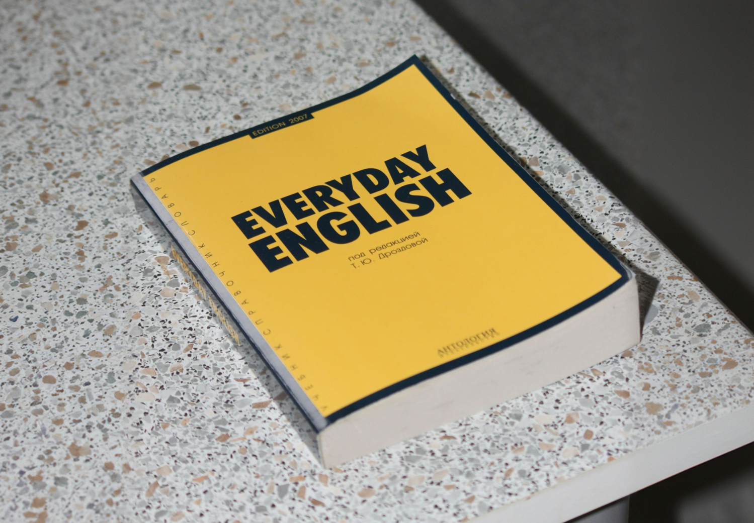 A yellow book entitled “Everyday English” lies on a speckled bench.