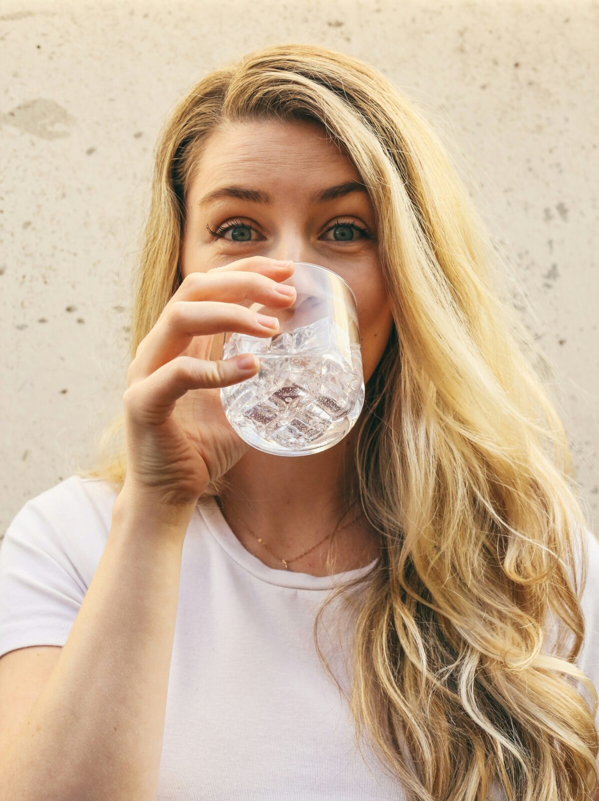 A young woman looking directly at the camera drinks water from a glass.