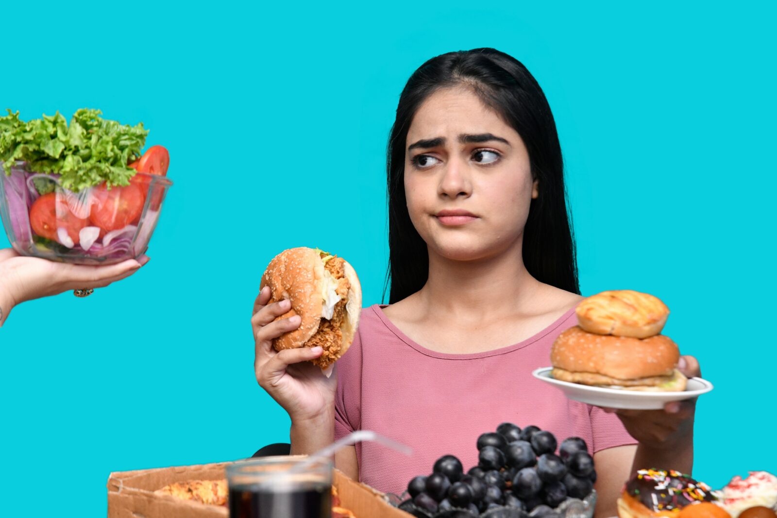 A young woman holds two burgers and looks quizzically at a salad