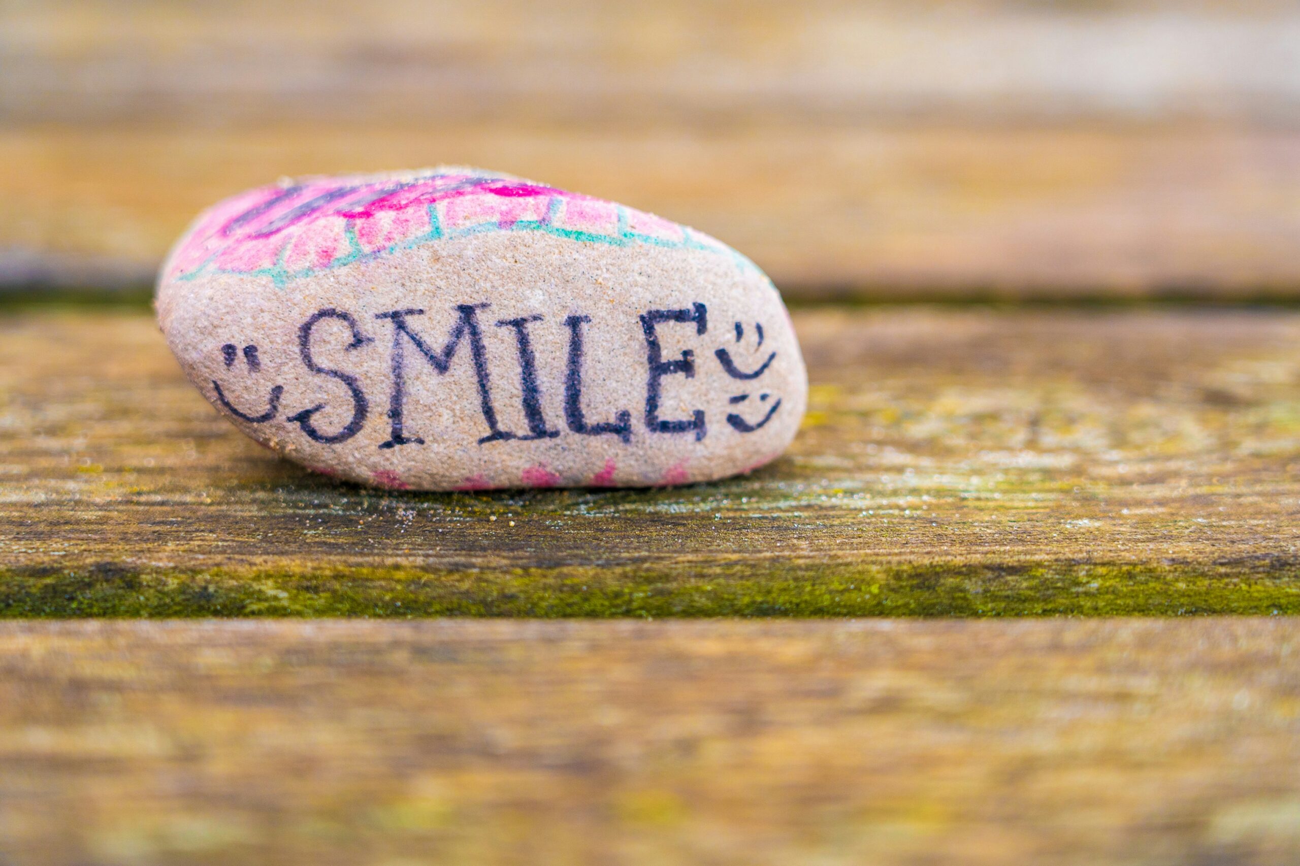 A stone sits on a wooden surface. On it is written ‘SMILE’.
