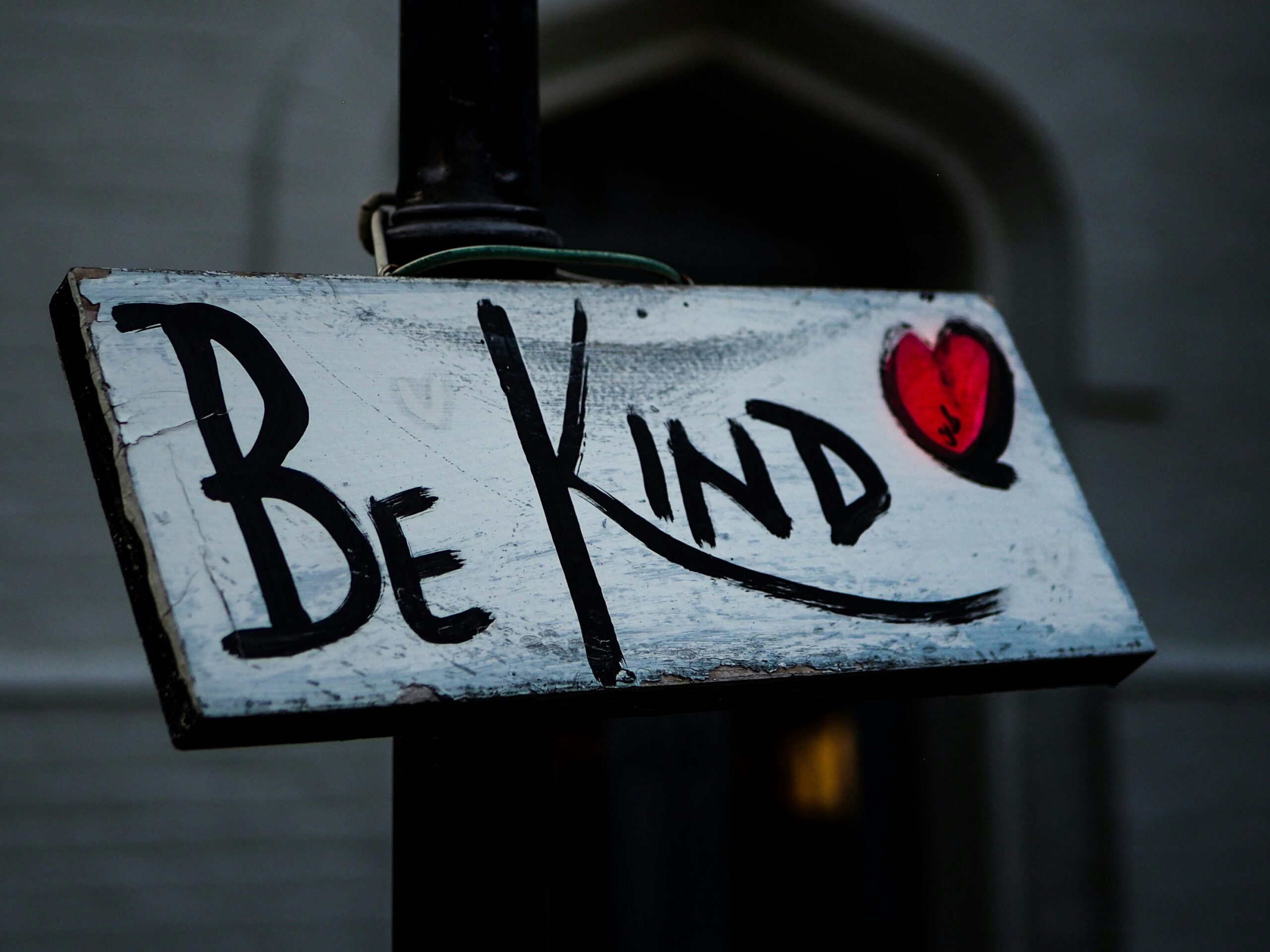 A white sign with black writing reads, “Be Kind” followed by a red heart.