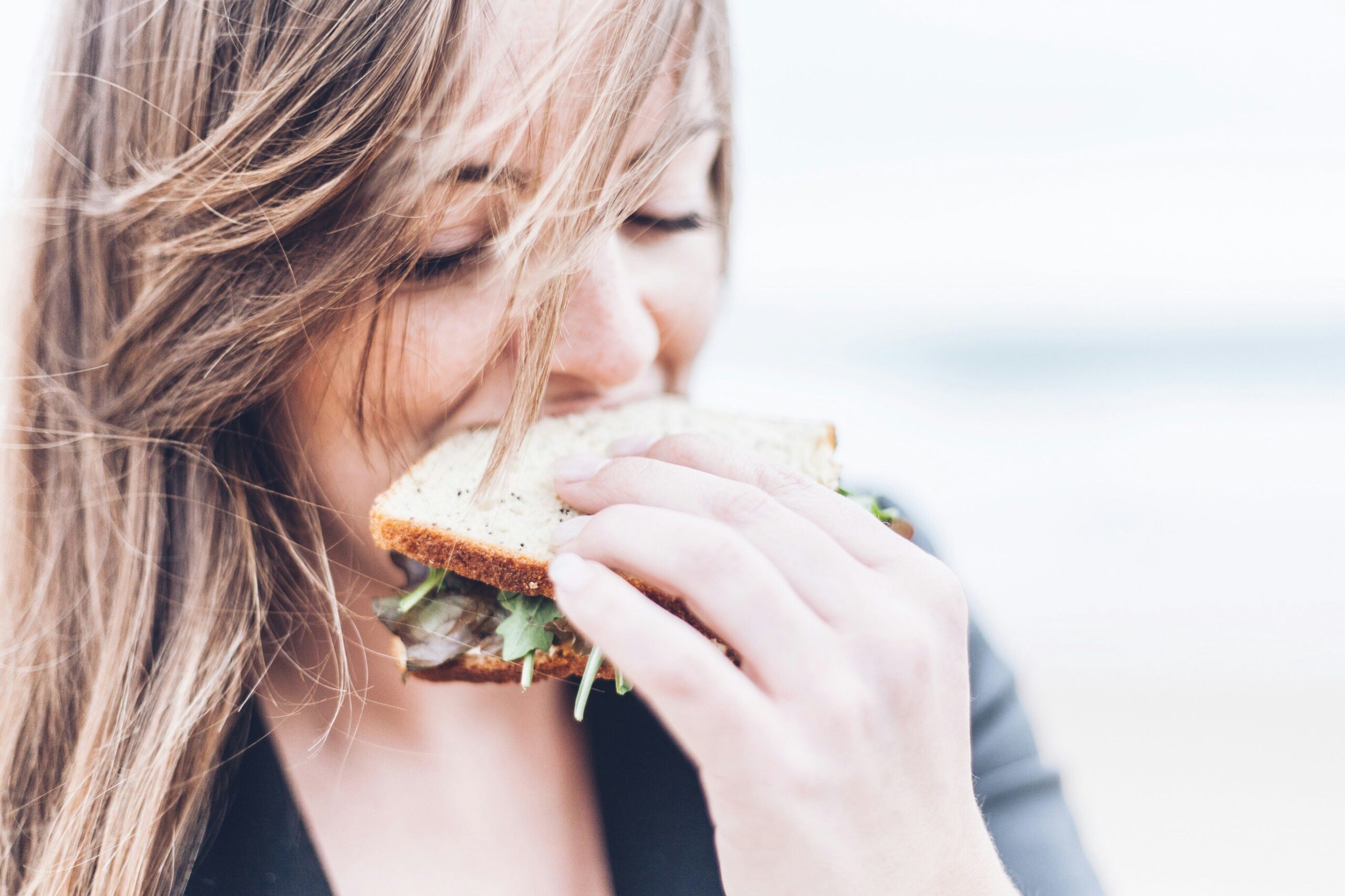A blonde woman bites into a sandwich